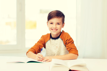 Naklejka premium smiling student boy writing to notebook at home