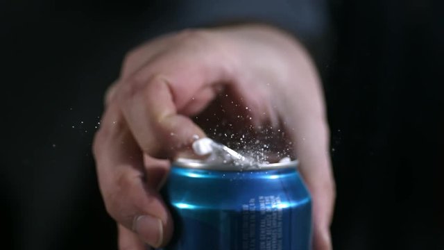 Extreme slow motion liquid spray as aluminum can tab is opened, closeup.