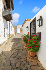 Fototapeta na wymiar Narrow street in Betancuria village with Santa Maria church tower in background, Fuerteventura, Canary Islands, Spain
