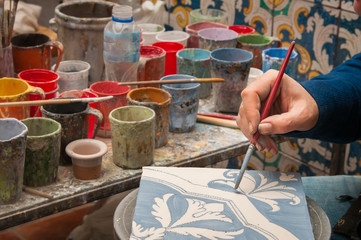Pottery artisan in Caltagirone, Sicily, decorating just enamelled square tiles in his work table