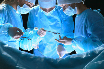Group of surgeons at work in operating theater toned in blue. Medical team performing operation - obrazy, fototapety, plakaty