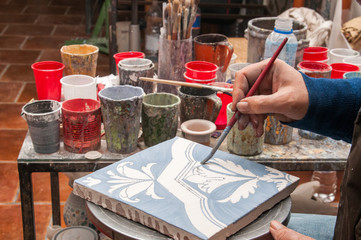 Pottery artisan in Caltagirone, Sicily, decorating just enamelled square tiles in his work table