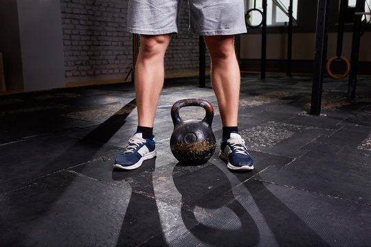 Cropped image of young man, legs in shorts and kettlebell. Crossfit workout theme on grey background.