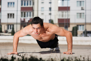 Obraz premium Portrait of strong young athlete push-uping outdoor in the courtyard