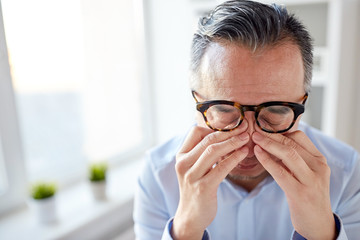 businessman in glasses rubbing eyes at office