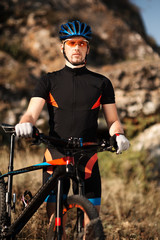 Portrait of male athletic standing with mountain bike in the hill with background of rock