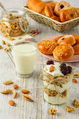 Healthy breakfast ingredients. Homemade granola with yogurt in open glass jar, milk and fresh fragrant buns. The food is rich in useful carbohydrates, vitamins and nutrients.