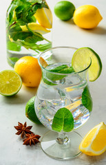 Homemade refreshing summer lemonade in a glass with lime, lemon and mint on a white concrete or stone  background.