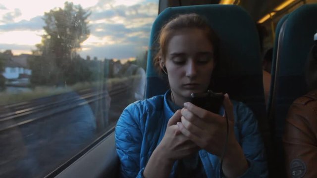 Young brunette beautiful girl using smartphone, sitting near the window in the train.