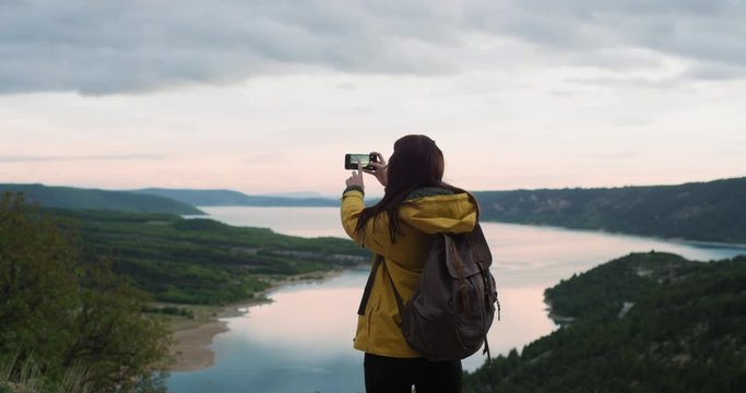Woman taking photograph of lake at sunrise smartphone photographing scenic landscape nature background view enjoying vacation travel adventure
