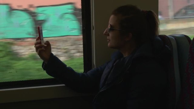 Young woman taking selfie photo with cellphone sitting on train or bus 