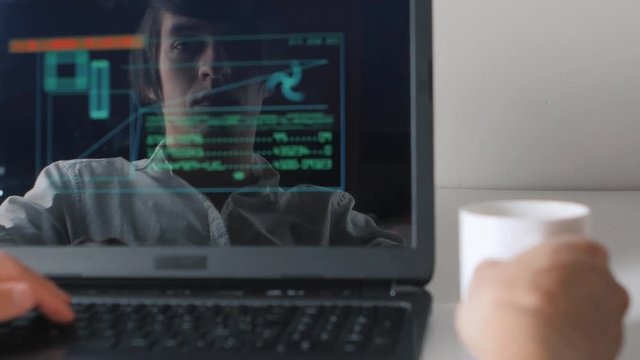 Reflection in the monitor the programmer works at the computer and drinks coffee. Double exposure.