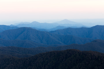 A layered mountain range stretches into the distance under a pastel coloured sunset sky.