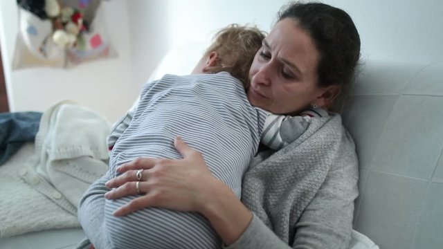 Mother With Concerned Look In Her Face Helping Baby Boy To Sleep