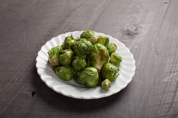 Small white plate of cooked green brussel sprouts on dark wooden background horizontal shot