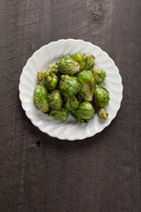 Small white plate of cooked green brussel sprouts on dark wooden background above shot