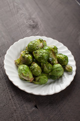 Small white plate of cooked green brussel sprouts on dark wooden background slightly above shot