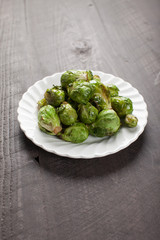 Small white plate of cooked green brussel sprouts on dark wooden background vertical shot