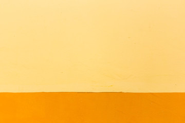 Aged concrete wall painted in orange and yellow colour.