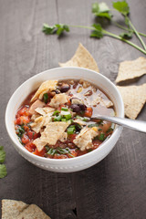 Homemade Taco Soup in small white bowl with crushed tortilla chips on dark wooden background angled shot