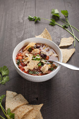 Homemade Taco Soup in small white bowl with crushed tortilla chips on dark wooden background vertical shot