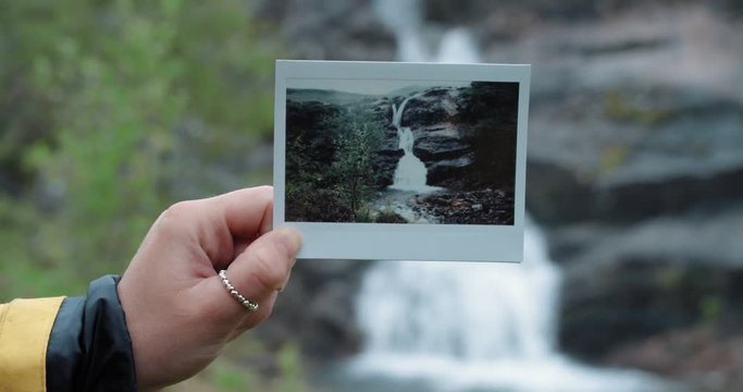 Hand holding instant photo of travel destination waterfall