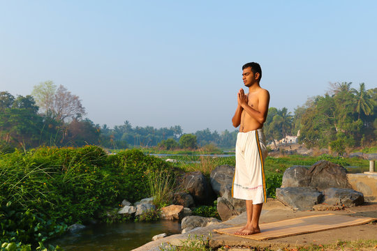 An Indian yogi performing yoga asanas on a riverbank in India.