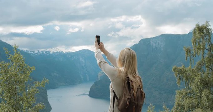 Woman taking panorama photograph fjords with smartphone photographing scenic landscape from high up nature background view enjoying Norway vacation travel adventure