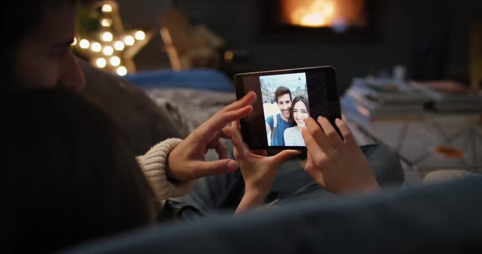 Closeup of couple using digital tablet by fireplace viewing honeymoon travel photos on touch screen browsing social media sharing wanderlust inspiration on digital device