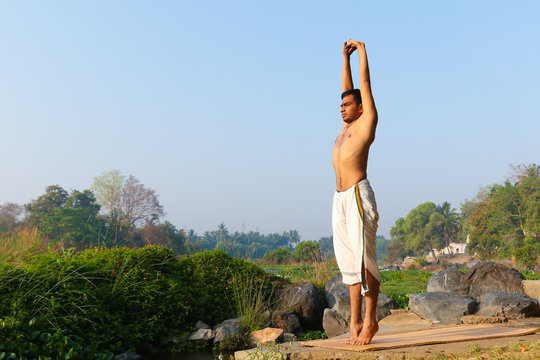 An Indian yogi performing yoga asanas on a riverbank in India.