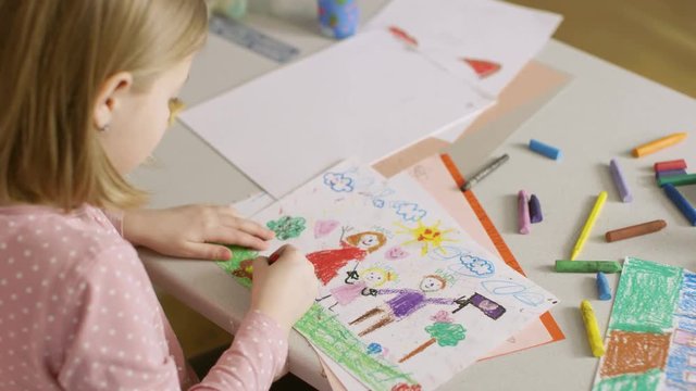 Over The Shoulder View of Cute Little Girl Drawing Her Family with Crayons. Shot on RED EPIC-W 8K Helium Cinema Camera.