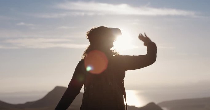 Hiker woman watching sunrise wearing virtual reality headset outdoors mountain top arms outstretched watching 360 video imagination concept
