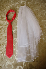 Bridal veil lies next to the red tie of the groom on the bed