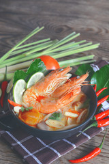 steamy hot famous thai cuisine tom yum goong soup served in ceramic bowl on wooden table.