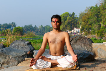 An Indian yogi meditating on a riverbank in India.