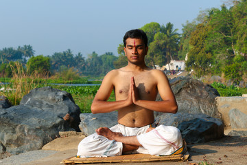 Naklejka na ściany i meble An Indian yogi meditating on a riverbank in India.