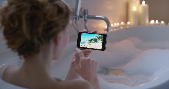 Beautiful Woman lying in bathtub using smartphone browsing social media inspirational travel photos mindfulness travel concept having bubble bath