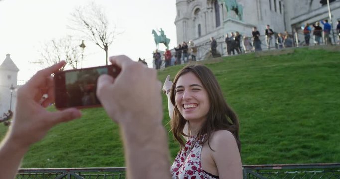 Tourist couple sightseeing man taking photograph of girlfriend pointing at  Sacre Coeur Paris enjoying summer holiday European vacation travel adventure 