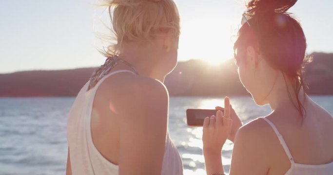 Women Taking Pictures with of Sunset with smartphone best friends on the beach near the Sea enjoying summer Vacation