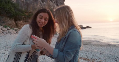 Two girl friends taking photograph of sunset on empty beach smartphone women photographing sunrise scenic landscape nature background view enjoying vacation travel adventure - Powered by Adobe