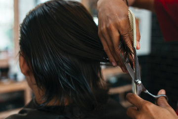 Close up of man that getting haircut by hairdresser with scissors and comb while sitting in chair. Barber shop