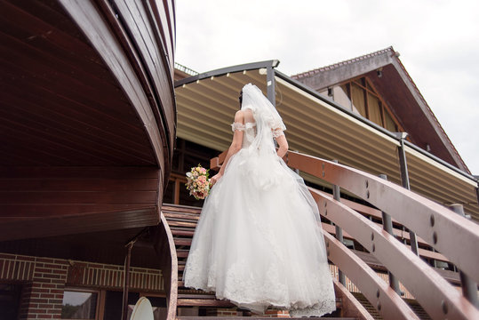 Bride in white wedding dress with bouquet in hand climbs the stairs