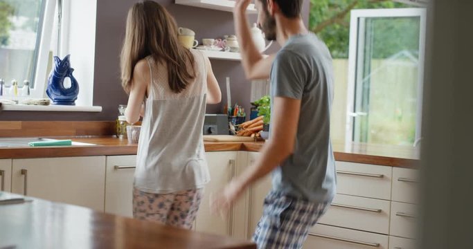 Happy young couple dancing in kitchen wearing pajamas ass wiggle listening to music morning at home having fun