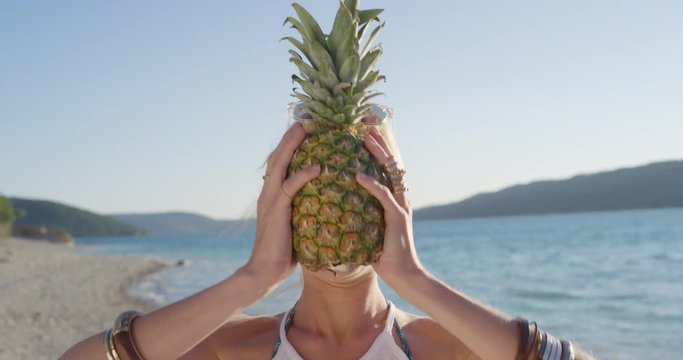 Close up attractive woman holding up pineapple posing for camera smiling laughing at sunset on tropical beach