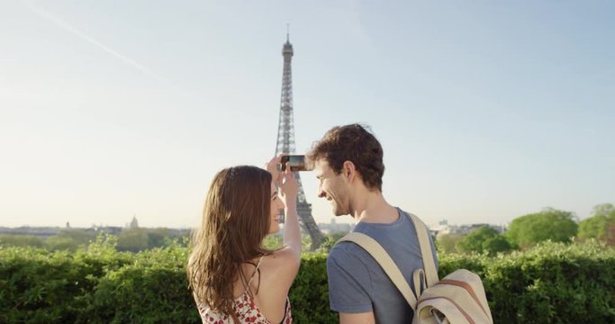 Tourist couple taking photograph of Eiffel Tower using smartphone at sunrise photographing scenic Paris cityscape background view enjoying European honeymoon vacation travel adventure