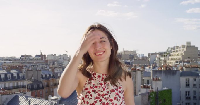 Close up portrait of beautiful young woman smiling laughing Paris city view from rooftop hair blowing in wind slow motion