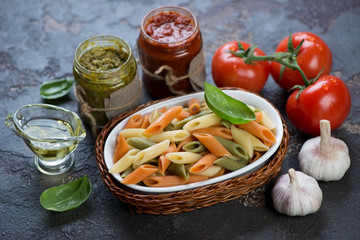 Three-colored penne pasta with different pesto sauces and cooking ingredients, closeup
