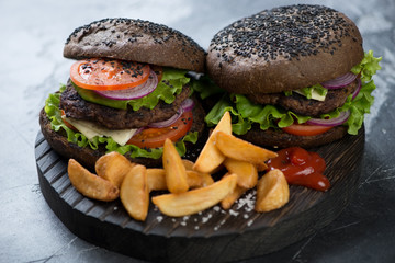 Close-up of two black beef burgers with potato wedges and ketchup, selective focus, studio shot