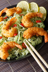 Fried shrimp with green pasta, chili, lime and sesame close-up on a plate. Vertical