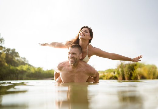 Shirtless man gives his wife a piggyback ride in the lake